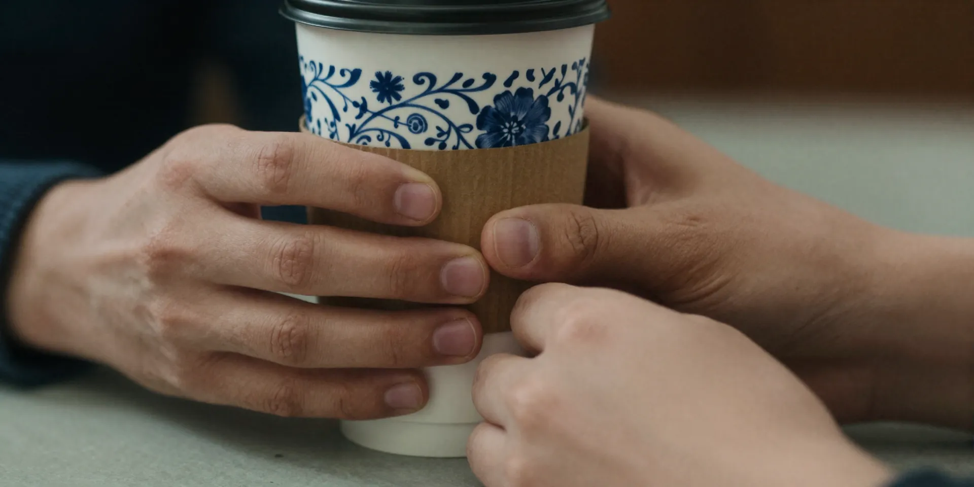 Close-up of two hands mid-conversation, one slightly fidgeting with a coffee cup sleeve. Ultra-detailed, shallow depth of field, texture of porcelain and paper, conveys micro-tension and humanity, shot on 35mm film --style raw