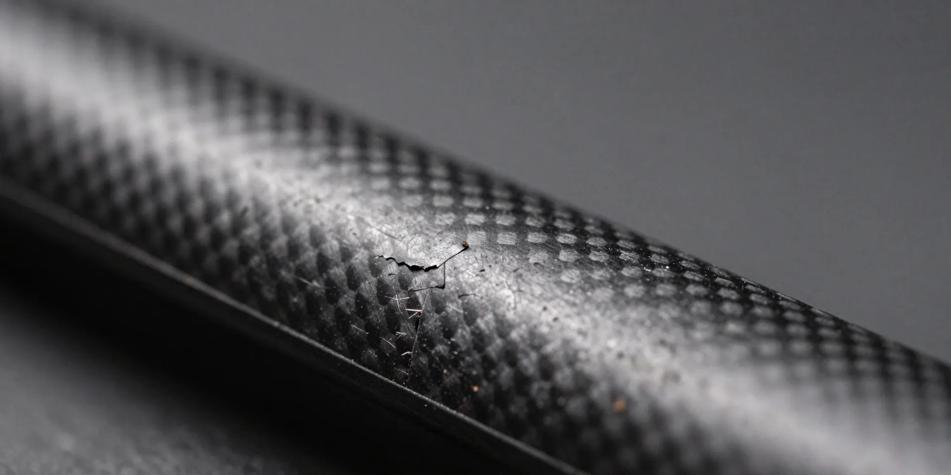 Macro photography of a scratched carbon fiber drone frame arm, revealing slight delamination at the tip, harsh side lighting highlighting the texture, ultra-realistic --ar 16:9