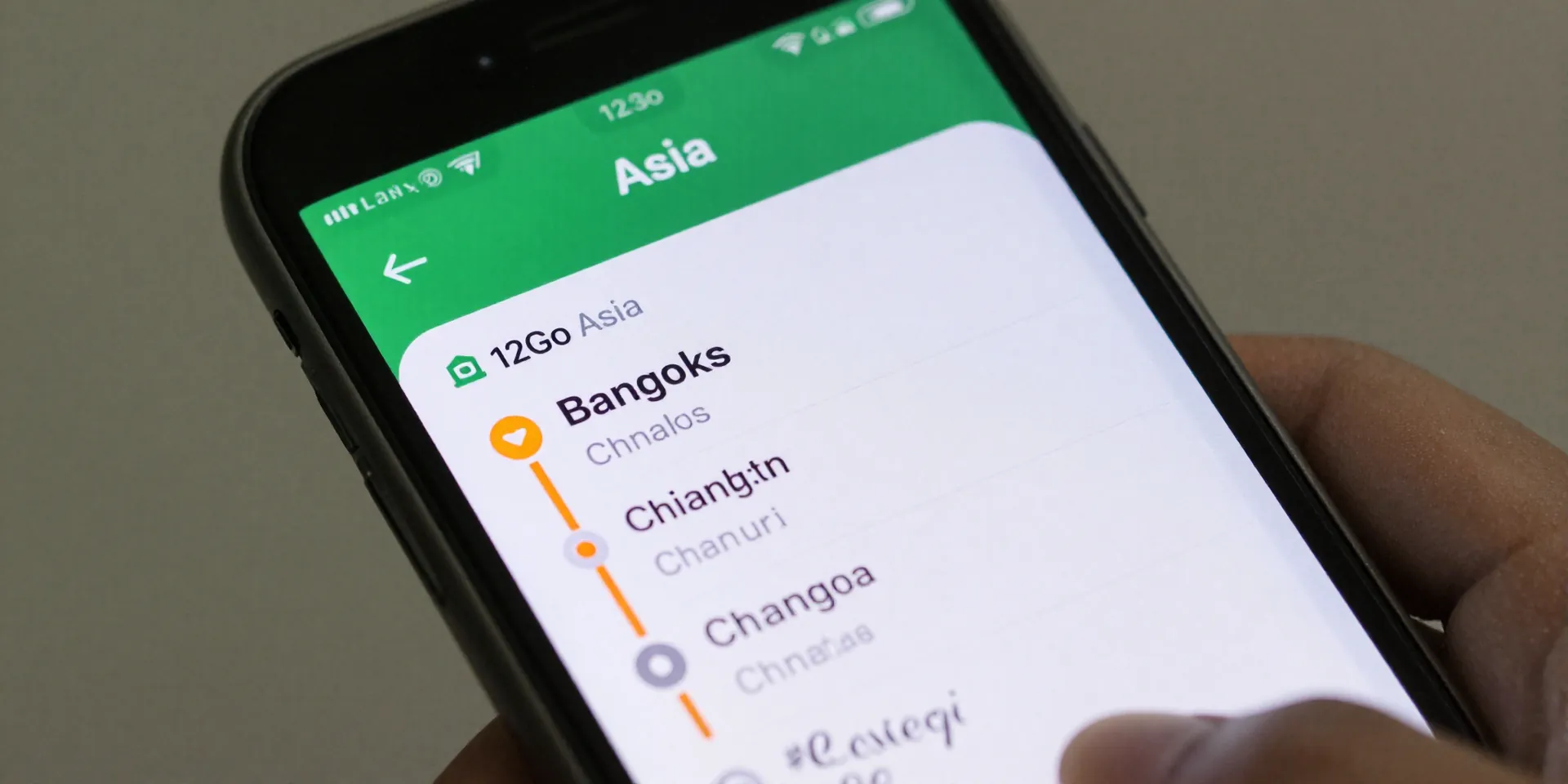 Close-up of a smartphone screen showing the 12Go Asia app interface, displaying bus routes from Bangkok to Chiang Mai. The screen is slightly dirty with fingerprints, held in a traveler's hand. Flat lay style, sharp focus --ar 4:3