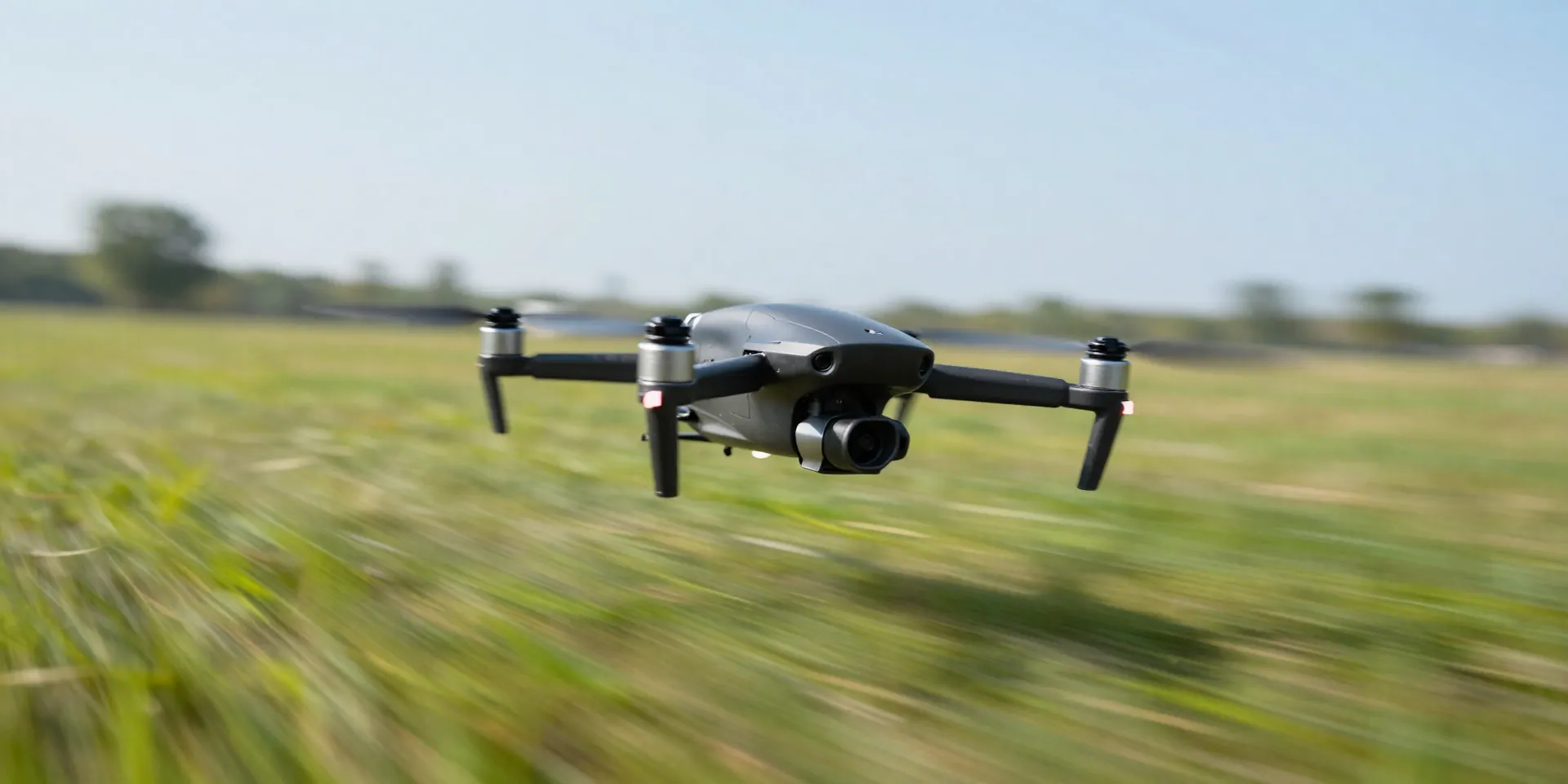 FPV drone flying aggressively low over a grassy field, heavy motion blur on the background, sharp focus on the drone, bright sunny day, action shot, --ar 16:9