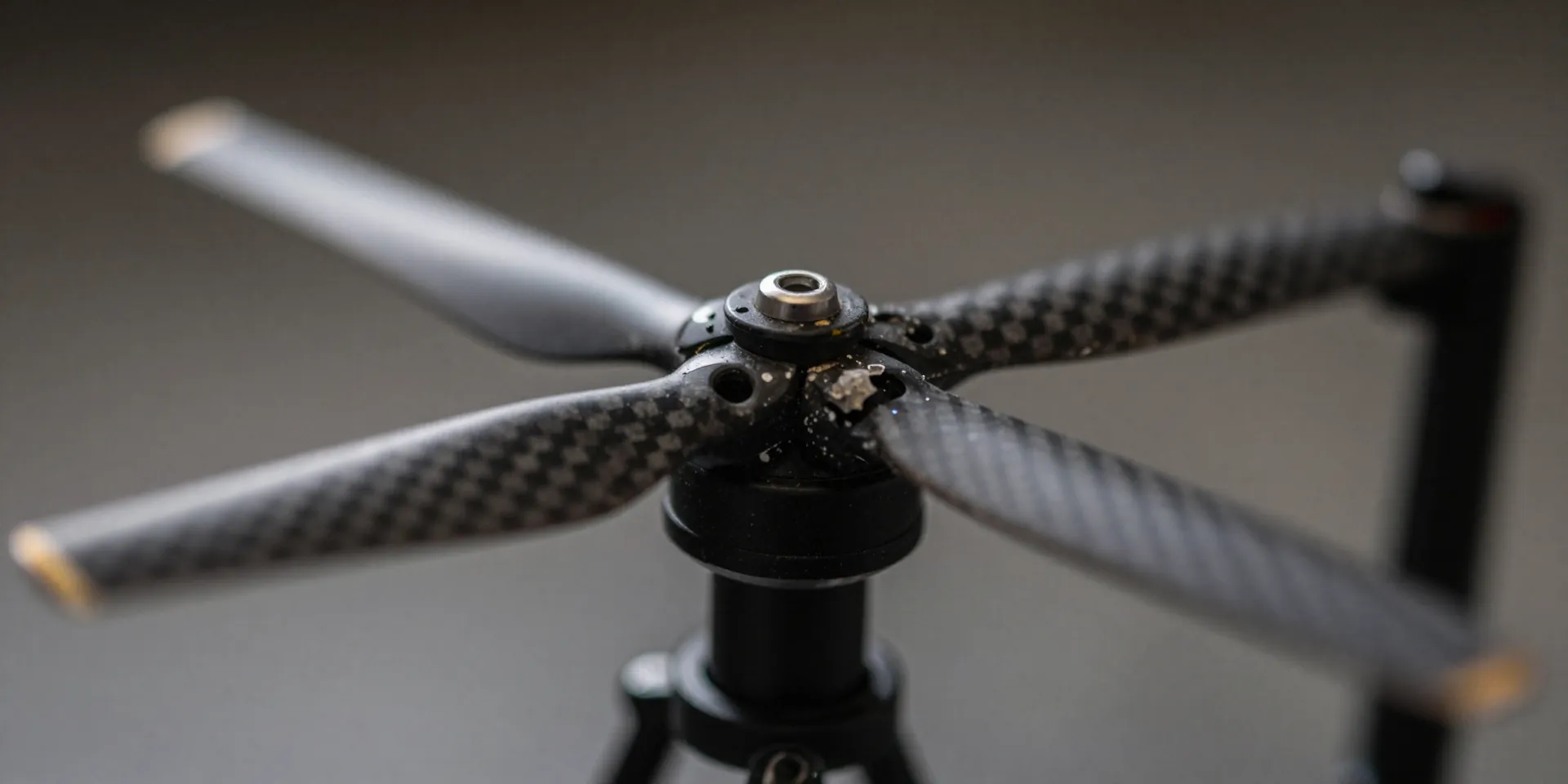 Macro photography of a chipped and dirty carbon fiber drone propeller spinning rapidly, motion blur, moody workshop lighting, photorealistic --ar 16:9