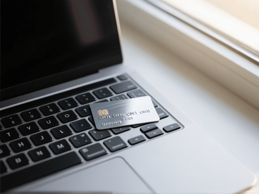 Looking down on a modern laptop keyboard, a sleek travel credit card placed on the 'enter' key. through a window, card's