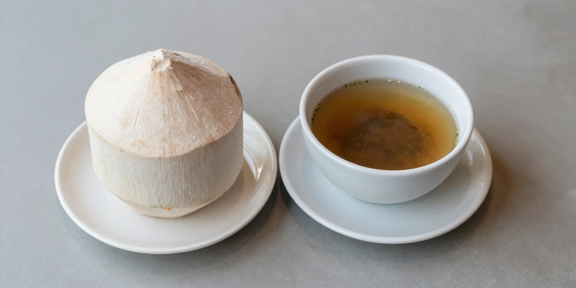 Close-up, overhead shot of a single place setting at a clean, modern Balinese cafe. A fresh coconut, peeled fruit on a plate, and hot soup in a bowl. Minimal, clean, safe aesthetic. –v 6.0