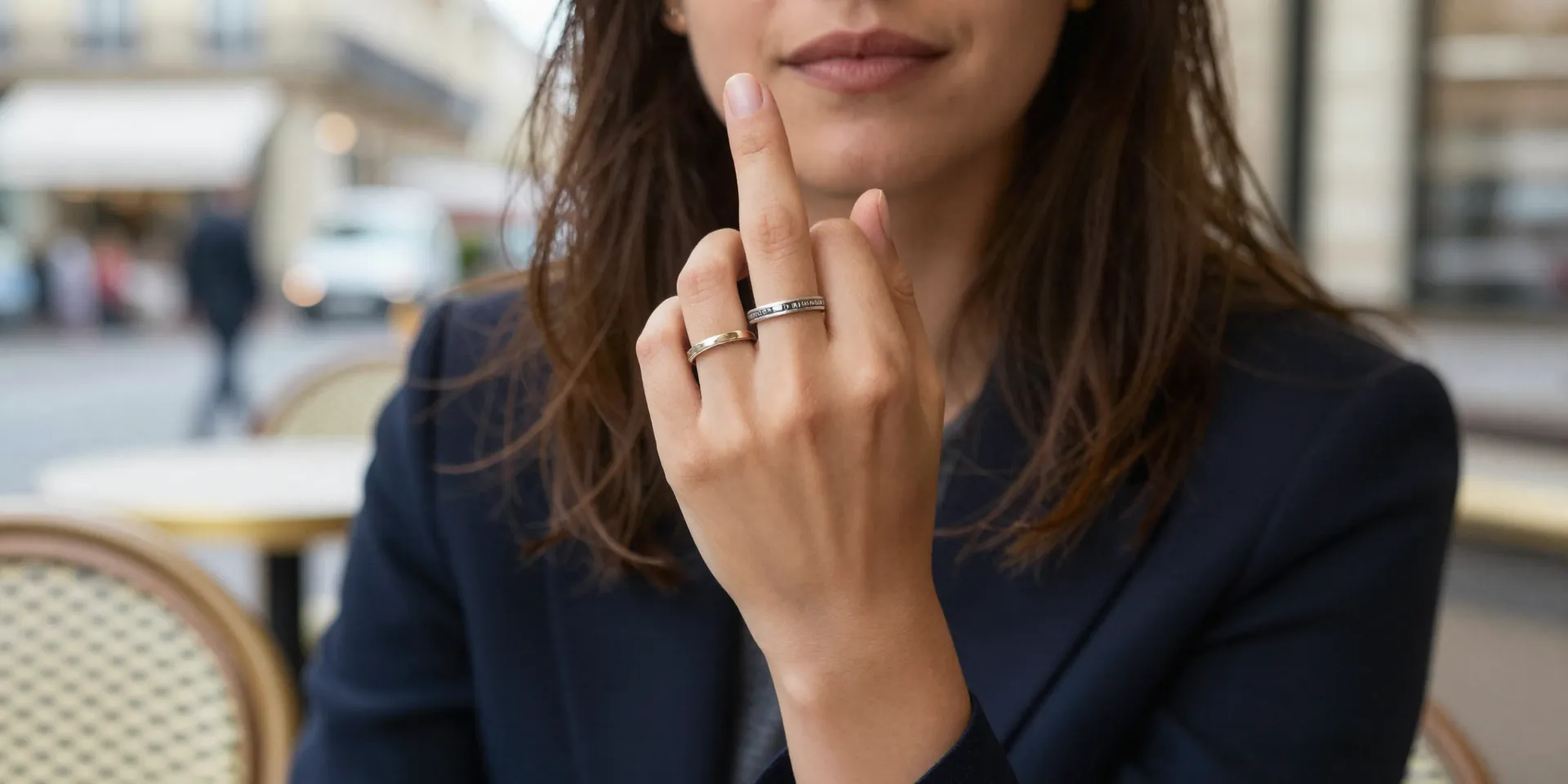 Close up of a female traveler holding up a fake cheap wedding ring on her finger while sitting at a Parisian cafe, street background blurred, soft natural lighting, candid shot --ar 16:9