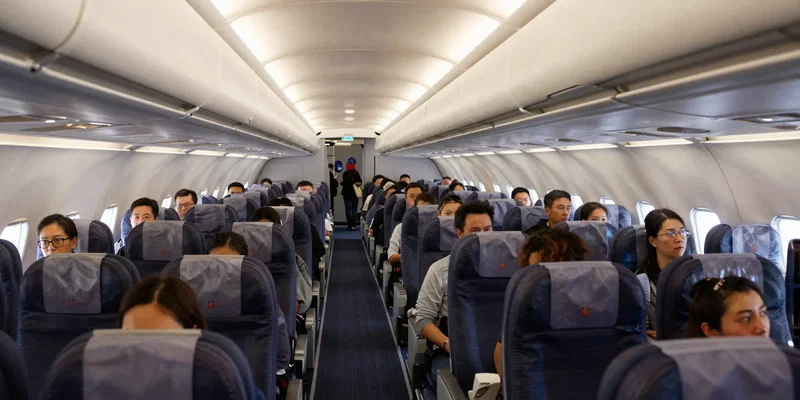 Wide-angle shot of a vibrant, low-cost airline cabin, all passengers seated, except for two lonely-looking travelers isolated in single middle seats rows apart, cinematic lighting --ar 16:9 --style raw --v 6.0
