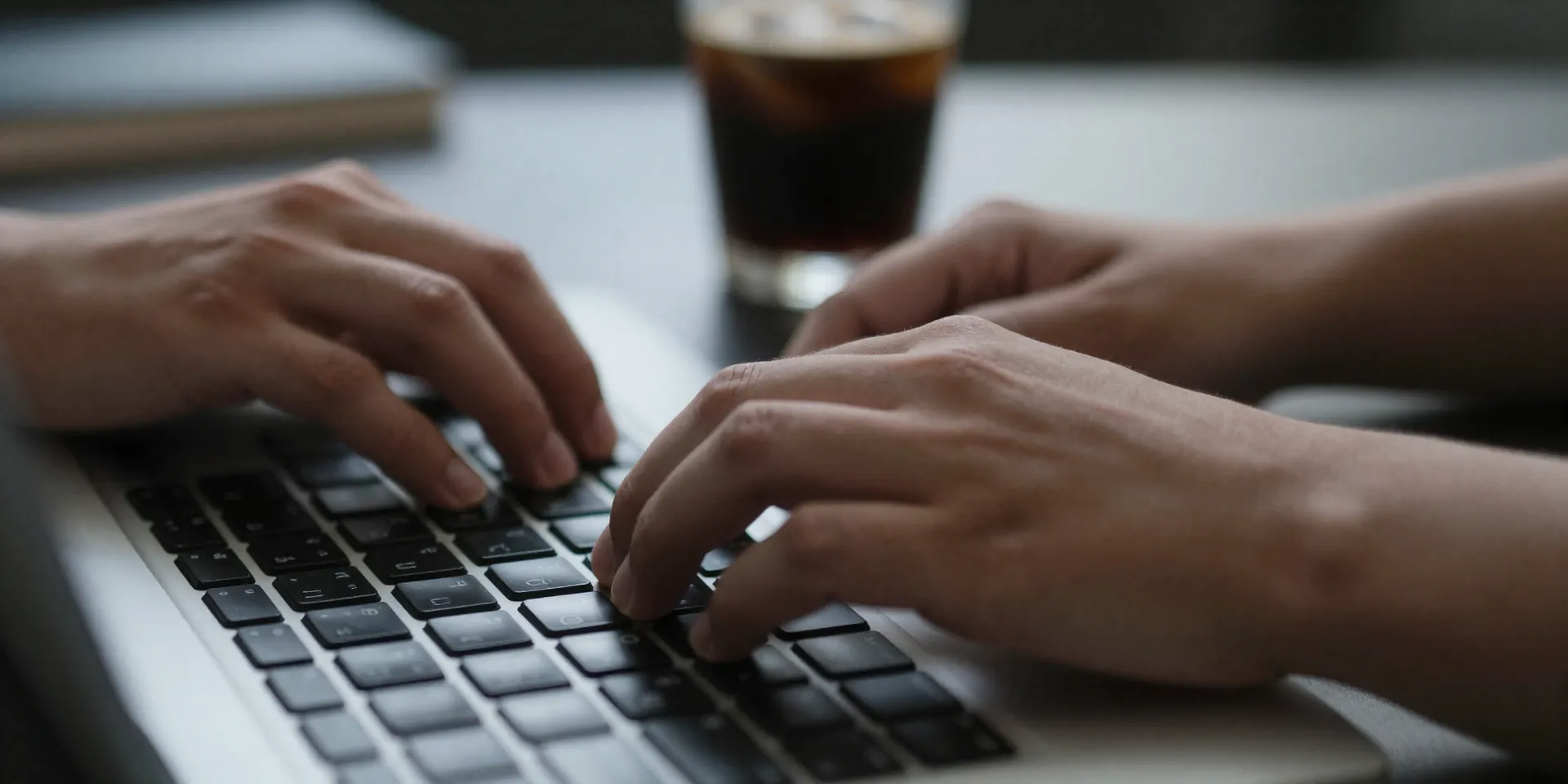 close up of hands typing on a keyboard, tension visible in the fingers, a cold cup of coffee sits forgotten to the side, shallow depth of field, moody morning light