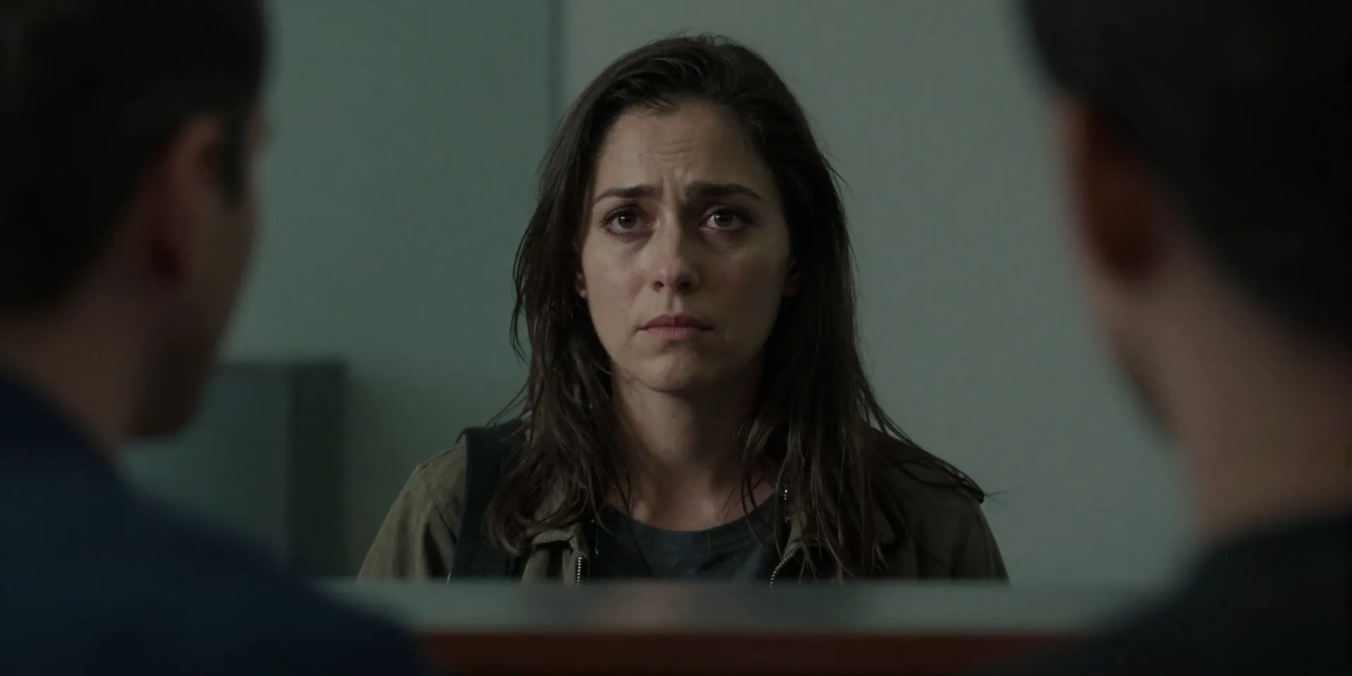 Medium close-up portrait of a weary solo traveler at a border counter, making calm, direct eye contact with an official whose face is slightly in shadow, neutral expressions, tension conveyed through body language, dramatic low-key lighting, cinematic, inspired by film stills