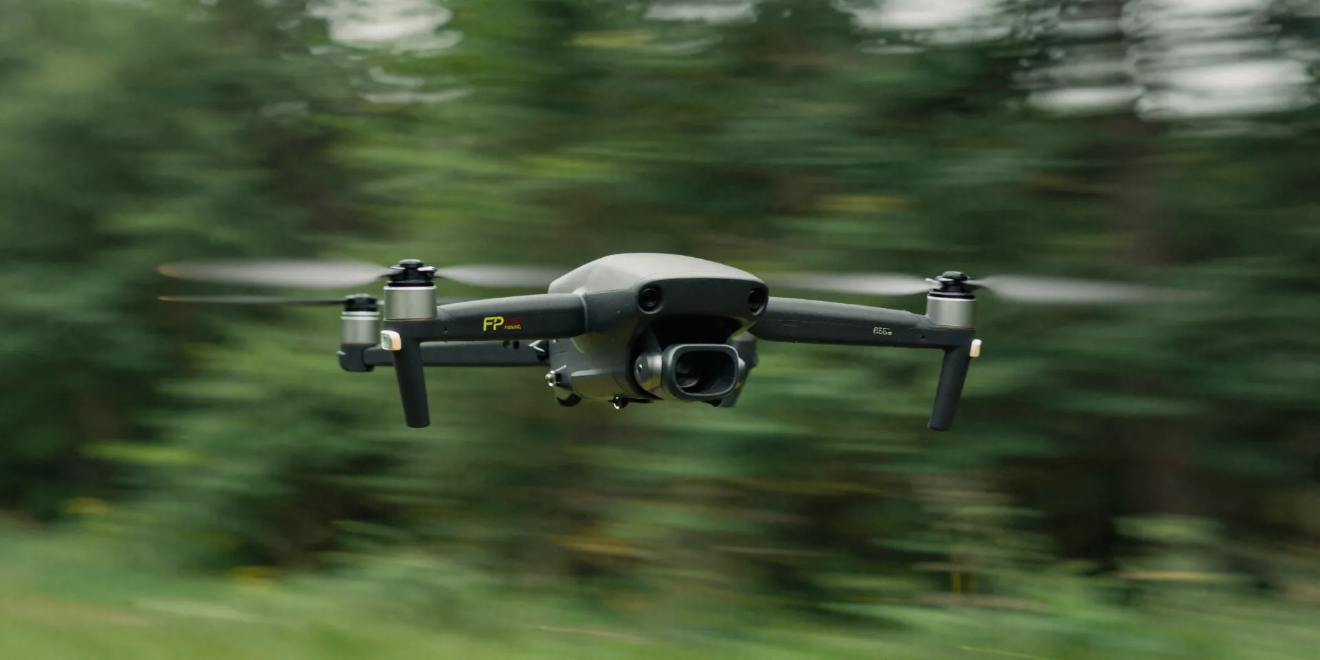 FPV drone flying low over a lush green forest, background dramatically blurred with motion streaks, sharp drone subject, cinematic color grading, hyper-realistic --ar 16:9